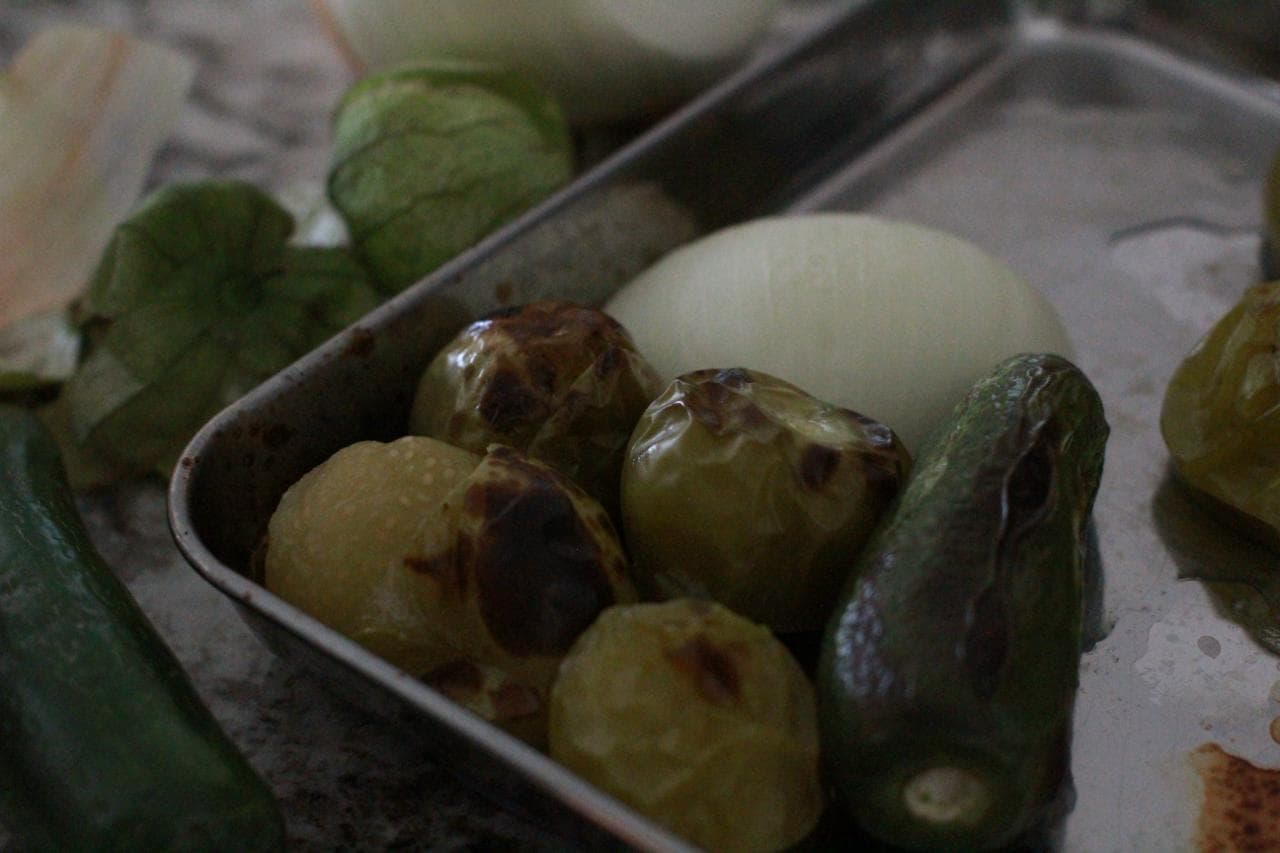 Close-up of blistered roasted tomatillos, jalapeño, and onion on a sheet pan